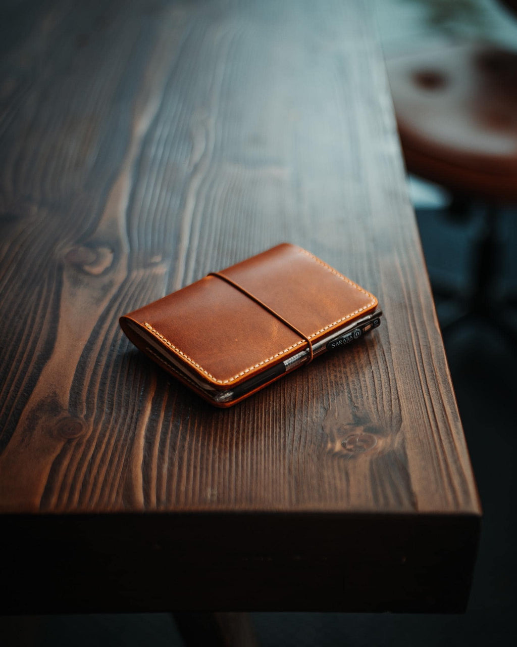 The Adventurer | Gloss in Amber Tan, closed with its elastic band on a wooden table